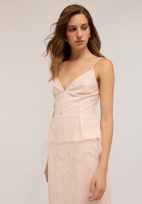 Vestido rosa empolvado con encaje, corpete ajustado, escote en V profundo y tirantes delgados. El detalle de peplum añade textura y forma a la silueta.