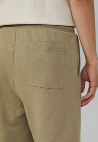 Olivgrüne Sweatpants aus einem strukturierten, weichen Stoff. Mit einer einzigen Gesäßtasche, die über detaillierte Nähte und ein geprägtes Logo verfügt.