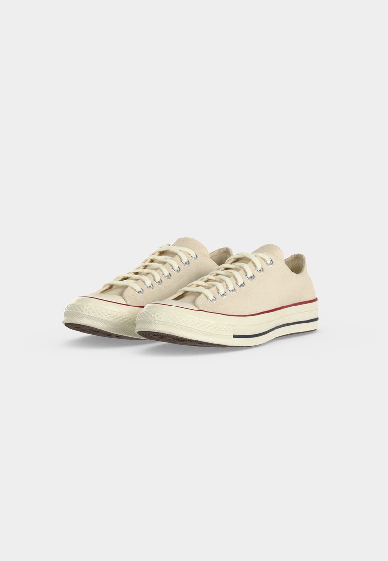 Coppia di sneakers basse beige in tela con lacci bianchi e suole in gomma crema con strisce rosse e nere.