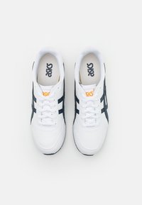 Bílé sportovní boty s námořnickými pruhy, s hladkým koženým svrškem, kulatou špičkou a polstrovaným límcem. Logo ASICS v černé a oranžové barvě.