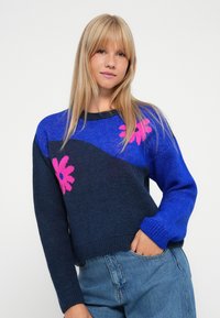 Knitted sweater with navy base, blue accents, and bright pink flower patterns. Features ribbed cuffs and hem, round neckline, and a relaxed fit.