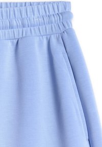 Pantalon de survêtement en tissu bleu clair avec une ceinture élastique et une poche latérale avec des coutures visibles sur fond blanc.