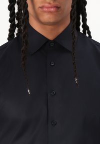 Navy button-up shirt with a pointed collar, featuring a smooth texture and visible buttons along the front. Two braids frame the face.