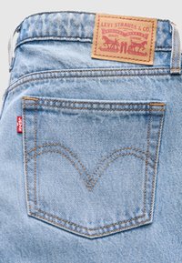 Poche arrière d'un jean en denim bleu clair avec des coutures orange, un onglet rouge Levi's et un patch en cuir beige marqué Levi Strauss & Co. au-dessus de la ceinture.