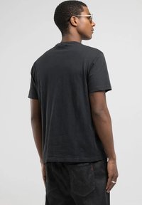 Camiseta de algodón negra con cuello redondo y mangas cortas, que presenta una textura suave y un ajuste relajado, mostrada desde la parte de atrás.