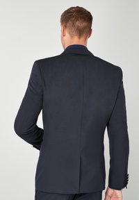 Giacca da abito blu navy con una sola apertura, spalle strutturate e polsini a tre bottoni. Tessuto liscio e strutturato, design sartoriale per un aspetto formale.