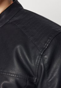 Chaqueta de cuero negra con una textura suave, acentos acolchados en los hombros y un cuello estructurado. Diseño clásico con detalles mínimos.