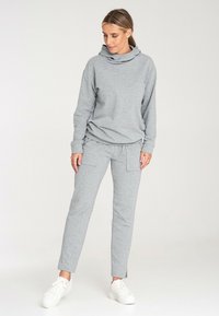 Szara bluza z kapturem o wysokiej szyi i długimi rękawami, zestawiona z szarymi zwężającymi się spodniami z bocznymi kieszeniami. Oba elementy wykonane z miękkiego materiału.