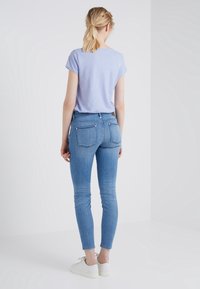 Ljusblå kortärmad T-shirt kombinerad med figurnära ljusblå jeans med två bakfickor och vita sneakers, sedd bakifrån.