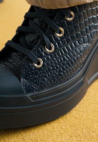 Baskets montantes noires en matériau synthétique texturé imitant le crocodile, avec œillets dorés, lacets noirs et semelle en caoutchouc.