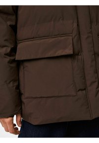 Bruzsā pūkā jaka ar teksturētu virsmu, lielu priekšējo kabatu un smalkām šuvēm. Piedurknē ir bezšuvju dizains.