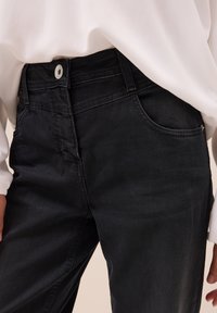 Zwarte denim jeans met een klassieke vijf-pocketdesign, riemlussen en een zilveren knoopsluiting. De stof heeft een gladde, iets gestructureerde afwerking.