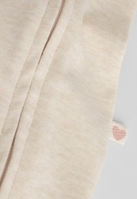 Tela de algodón beige con una textura suave, que presenta una pequeña etiqueta tejida con un diseño de corazón rosa en el borde. Simple y sin adornos.