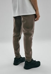Brązowe dresy o tapered designie z teksturowanej tkaniny, w połączeniu z czarnymi butami sportowymi. Stylizacja ma swobodny, sportowy wygląd.
