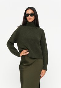 Oliven grønn genser med høy hals, myk tekstur, cropped design og lange ermer, kombinert med et matchende, elegant, gulvlangt skjørt.