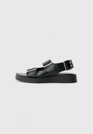 Sandale din piele neagră, cu două curele cu cataramă, talpă plată și un finisaj texturat. Designul este minimalist, având o talpă lată.