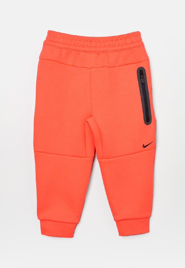 Spodnie dresowe dla dzieci Nike w jasnoczerwonym odcieniu, z elastycznym pasem, zwężającymi się nogawkami oraz kieszenią na zamek błyskawiczny z czarnymi detalami.