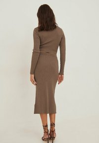 Robe midi brun côtelé avec des manches longues et une silhouette ajustée, accentuée par une taille ceinturée et des talons avec lanières.