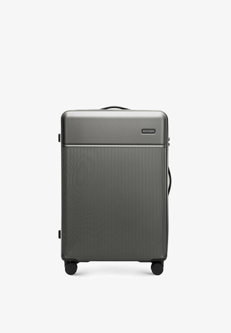 Hard-shell suitcase in dark gray with vertical ribbed texture. Features a top handle, zipper closure, and four black wheels for mobility.