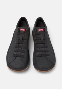 Scarpe nere casual con lacci elasticizzati e suola in gomma, con il logo rosso Camper sulla linguetta, su uno sfondo neutro.