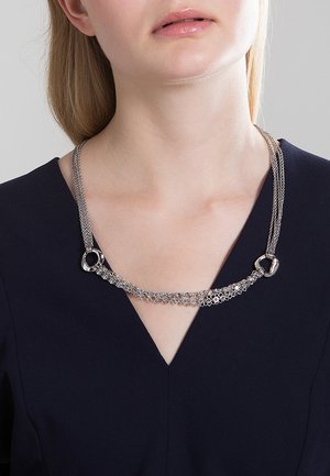 Sølvkæde med sammenkoblede designs, cirkulære accenter og teksturerede led, der elegant hænger rundt om halsen.