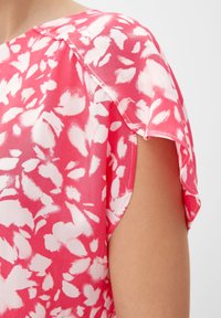 Blusa rosa realizzata in tessuto leggero, con un motivo floreale nelle tonalità del bianco, dotata di maniche corte e un design dalla vestibilità rilassata.