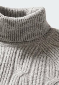 Pull à col roulé gris doux en maille côtelée montrant le col plié et les détails texturés du tissu sur le haut de la poitrine.