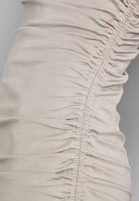 Beige stoff med rynkete tekstur langs sømmen, som viser en glatt finish og subtil glans. Egnet for tettsittende klesdesign.