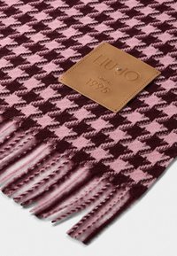 Sciarpa di lana con un motivo a scacchi in bordeaux e rosa. Presenta bordi frangiati e un'etichetta in pelle marrone con testo in rilievo.