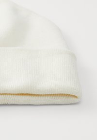 Cappello in maglia bianco con risvolto. Presenta una texture a coste, materiale morbido e una finitura liscia. Design semplice senza ulteriori pattern.