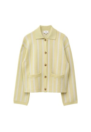 Femme portant un cardigan rayé jaune et blanc boutonné et une jupe assortie, tenant un sac à main noir, avec des lunettes de soleil foncées et des boucles d'oreilles créoles.