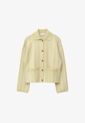 Femme portant un cardigan rayé jaune et blanc boutonné et une jupe assortie, tenant un sac à main noir, avec des lunettes de soleil foncées et des boucles d'oreilles créoles.