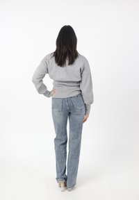 Maglione grigio in cotone con spalle scese, abbinato a jeans azzurri a vita alta con tasche posteriori. Texture morbide e vestibilità rilassata.