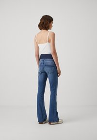 Blå flagrende jeans med en tettsittende linning, kombinert med en hvit camisole. Jeansene har baklommer og en lett falmet vask.