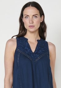 Top senza maniche blu navy con design floreale ricamato e bordino in pizzo. Presenta un collo a V e una texture plissettata per dettagli aggiuntivi.