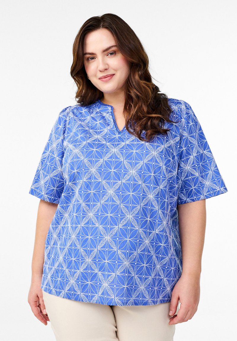 Blau gemusterte Bluse mit kurzen Ärmeln, V-Ausschnitt und geometrischem weißen Design. Hergestellt aus leichtem Stoff, mit weicher Textur.