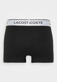 Black boxer shorts with a white elastic waistband featuring the brand name "LACOSTE." Smooth, stretchy fabric with a slight sheen.