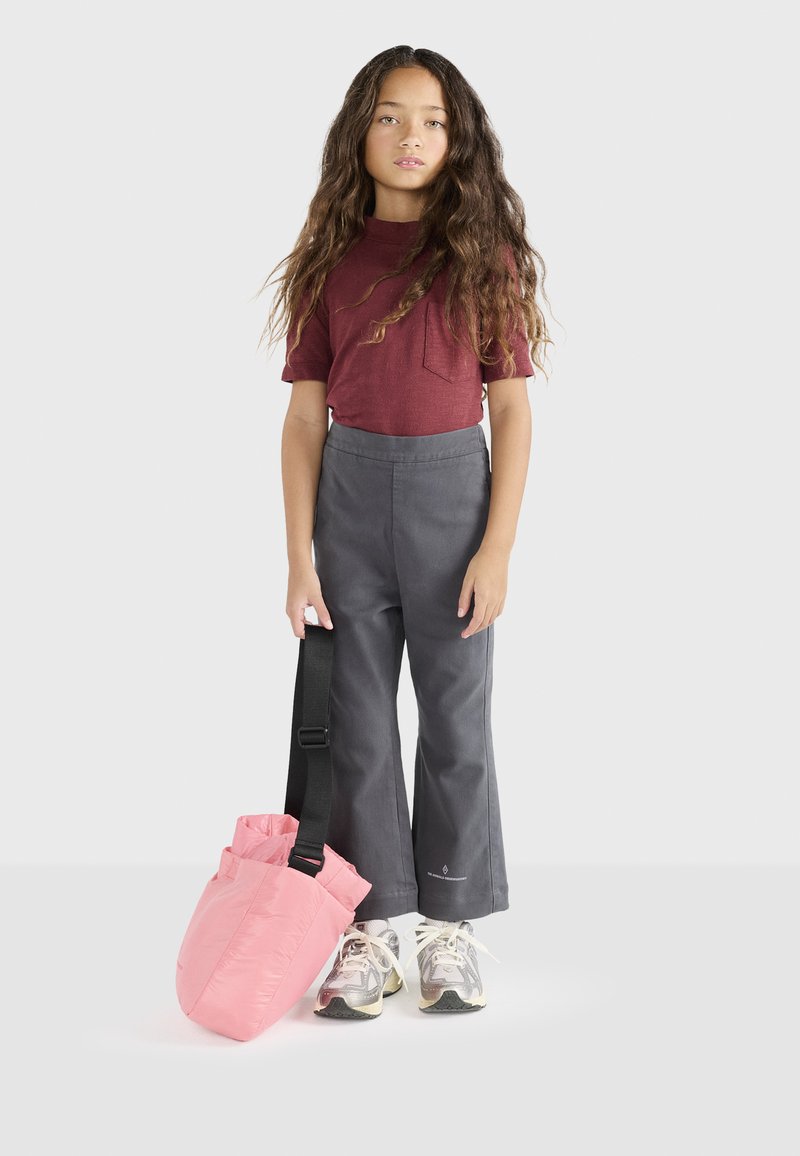 Sivé široké nohavice, vínová krátka rukávová košeľa s vreckom a ružová crossbody taška. Obuv je v kombinácii sivých a bielych tónov.