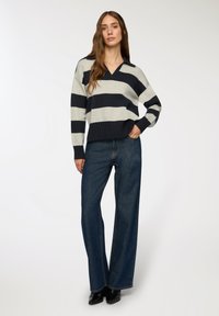 Pasiasty sweter w odcieniach szaro-niebieskich z dekoltem w kształcie litery V, prążkowanym hemem i długimi rękawami. Zestawiony z ciemnoniebieskimi dżinsami z wysokim stanem i fasonem dzwonowym.