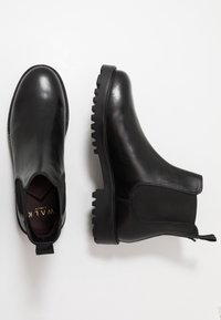 Botas Chelsea de cuero negro con paneles laterales elásticos, suela de goma texturizada y una pestaña en la parte superior para facilitar su uso. Acabado suave en general.