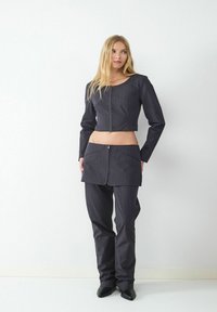 Dunkel gestreiftes Set, bestehend aus einer cropped Jacke mit rundem Ausschnitt und Reißverschluss vorne, kombiniert mit hochgeschnittenen Hosen und einem Minirock.