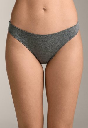 Nő egyszínű szürke bikini stílusú fehérneműben, hasát és felső combjait mutatva semleges háttér előtt.