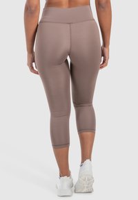 Leggings capri marroni a vita alta, realizzati in un tessuto elastico e liscio con un design aderente. Cuciture particolari e taglio a gamba affusolata.