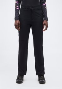 Άτομο με μαύρο παντελόνι ίσιας γραμμής, μαύρα αθλητικά παπούτσια και μακρυμάνικο μπλουζάκι με ροζ και μοβ αφηρημένα σχέδια στα μανίκια.