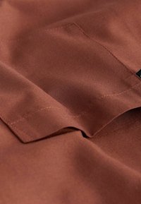 Nahaufnahme einer rostfarbenen Stofftasche mit sichtbaren Nähten und strukturierter Webart, die Falten und Schatten auf dem Material zeigt.