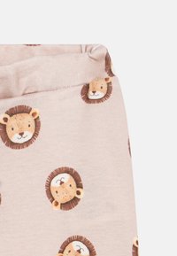 Pysjamasbukser laget av myk, lys rosa stoff med et gjentatt mønster av løvehoder med brune detaljer og runde ører.