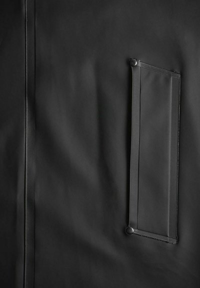 Zwart waterdicht stof met een gestructureerd oppervlak, voorzien van een verticale naad en een rechthoekige zak die met drukknopen is bevestigd.