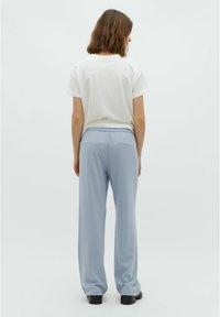 White short-sleeve T-shirt paired with light blue, wide-leg pants featuring an elastic waistband and two back pockets, viewed from behind.