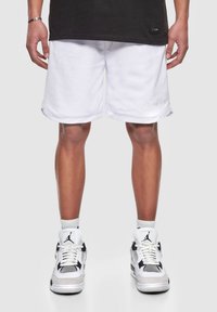 Shorts de sport blancs avec une texture en maille et un ourlet retroussé, associés à des baskets noir et blanc avec un logo marqué et des accents en maille.