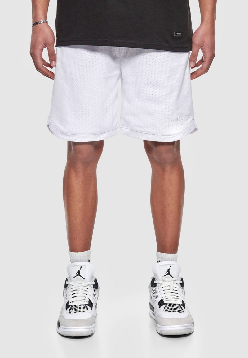 Hvide atletiske shorts med mesh-struktur og opbøgede kanter, parret med sort-hvide sneakers med fremtrædende logo og mesh-detaljer.